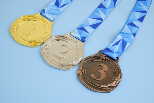 Gold, silver and bronze medal with ribbons on blue background close-up.