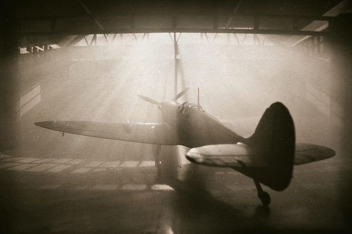 Sunlight streams through windows and reveals the iconic Mk Vc Supermarine Spitfire, seen here sitting in a traditional old aircraft hangar from WWII. Scale model photography.