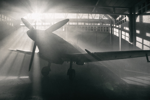 Sunlight streams through windows and reveals the iconic Mk Vc Supermarine Spitfire, seen here sitting in a traditional old aircraft hangar from WWII. Scale model photography.