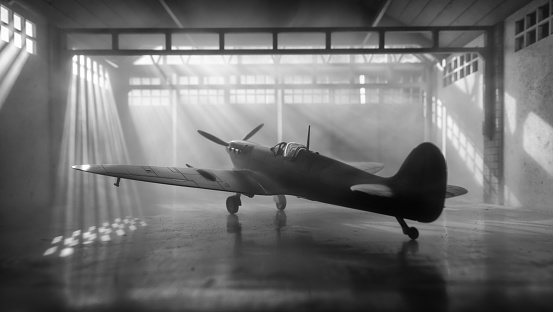 Sunlight streams through windows and reveals the iconic Mk Vc Supermarine Spitfire, seen here sitting in a traditional old aircraft hangar from WWII. Scale model photography.