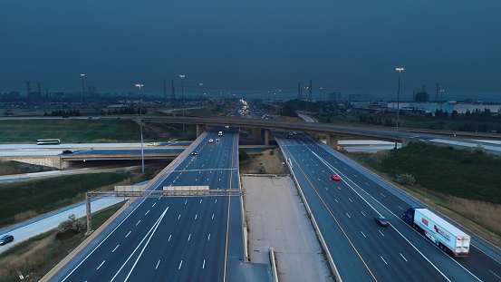 Drone flight over freeway as cars move swiftly, dark storm clouds gather ominously above, signaling an impending storm. Freeway under by nature's fury. Freeway view captures impending storm.