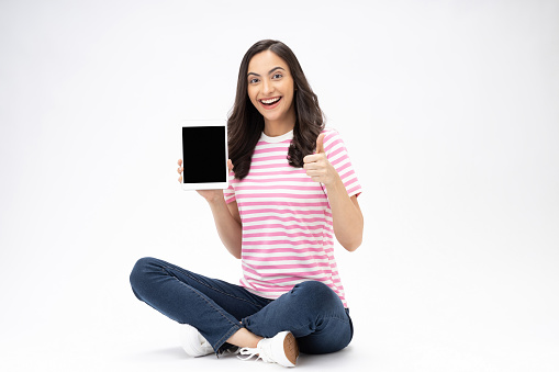 Full size photo of pretty young girl sit floor showing device screen wear trendy outfit isolated on white background