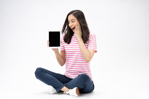 Full size photo of pretty young girl sit floor showing device screen wear trendy outfit isolated on white background