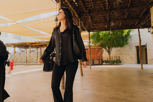 Low-angle view of female in black casual clothes walking the old streets with authentic Persian buildings at Al Bastakya district of Dubai city, United Arab Emirates