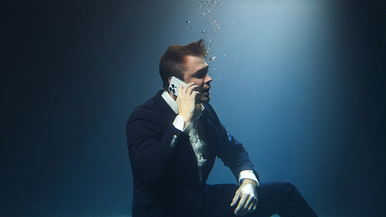 Businessman, a man in a suit, is talking on a mobile phone underwater