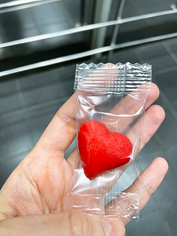 hand holds a red candy in a transparent heart-shaped package.