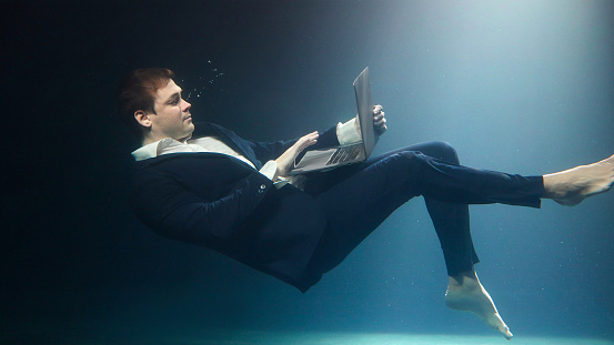 Businessman in a suit is working on a laptop and drowning under water