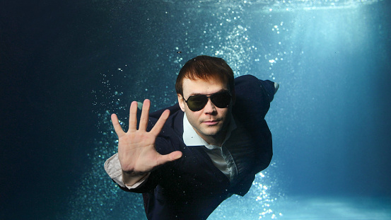 A man in a suit and sunglasses swims underwater to meet success