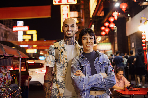 Young happy couple of tourists standing on the street and night and looking at camera.