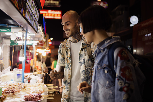 Young happy couple buying food on a street market at night.