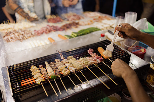 Close up of unrecognizable worker grilling variety of street food on a night market.