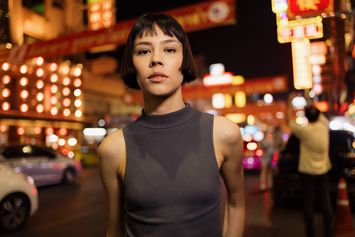 Portrait of carefree Asian model standing on the city street at night and looking at camera.