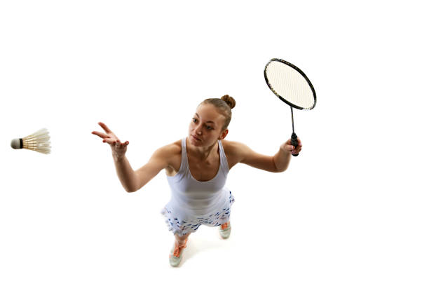 Top view dynamic image of young girl in uniform playing badminton, training isolated over white background. Concept of professional sport, active lifestyle, hobby, game, competition