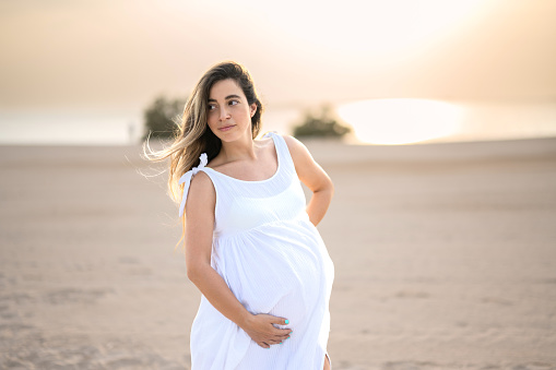 Portrait of beautiful pregnant woman in white dress on the beach
