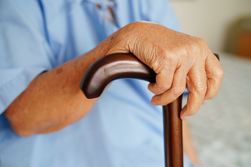 Asian elderly disability woman patient holding walking stick in wrinkled hand at hospital.