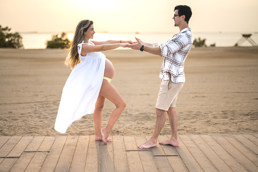 Beautiful young pregnant couple holding hands on beach