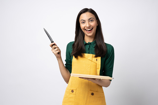 Indian woman chef wearing apron and holding cutting board while standing isolated on white background