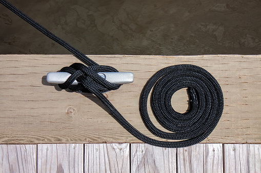 A black mooring rope with a knotted end tied around a cleat on a wooden pier.