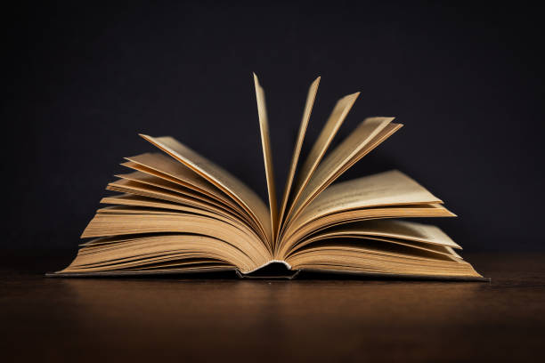 istock Open old book lying on a wooden table. Dark background 2086245742