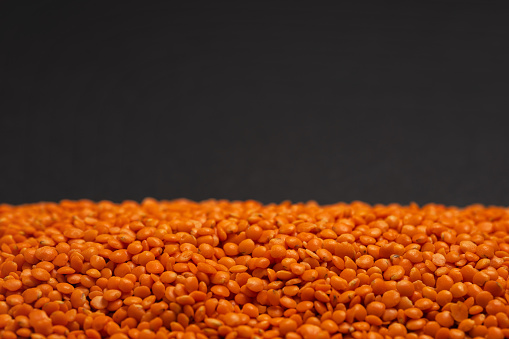 Red lentils pile. Dry orange lentil grains, heap of dal, dhal, masoor, Lens culinaris or Lens esculenta on dark background.