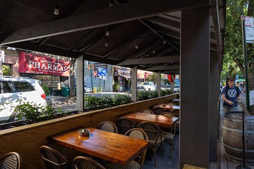 The Bronx, New York, USA – September 21th, 2023: Covered terrace along the sidewalk of Arthur Av in The Bronx New York. Wooden chairs and tables await customers.