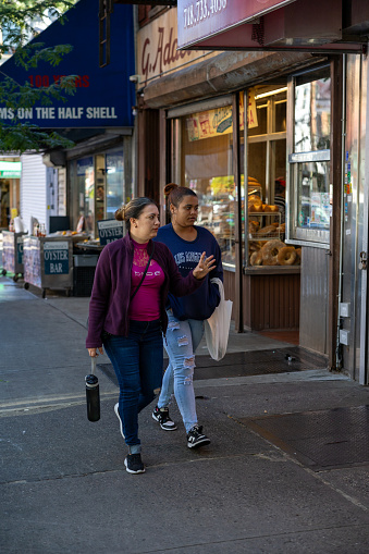 The Bronx, New York, USA – September 21th, 2023: Two ladies walk on Arthur Avenue in The Bronx New York and look at the shop windows