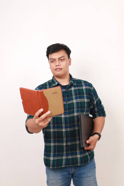 istock Young asian college student reading a book while holding a laptop 2086270170