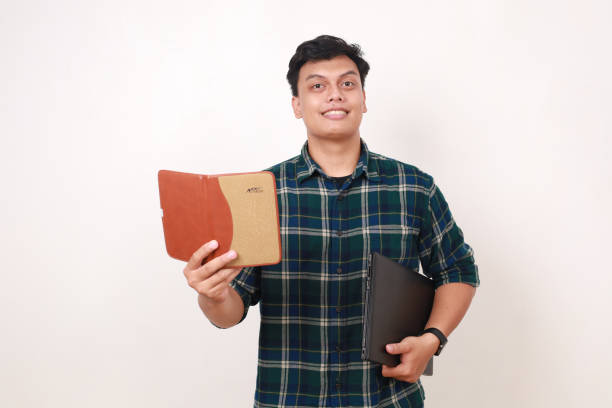 istock Young asian college student holding a book and a laptop with happy face expression 2086270696