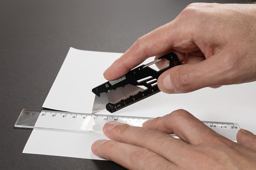 Man cuts paper with a stationery knife and ruler close up.