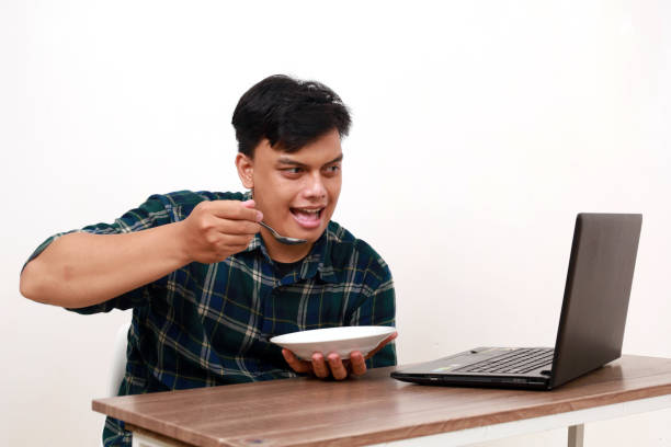 Confident young asian man eating while watching movie on his laptop