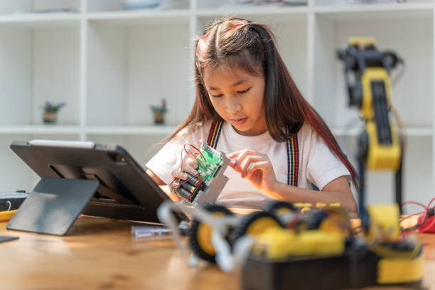 istock Smart young girl using small tool to put together her robot kit while following instructions from her computer tablet 2086283357