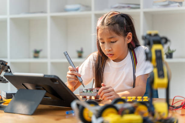 istock Smart young girl using small tool to put together her robot kit while following instructions from her computer tablet 2086283449