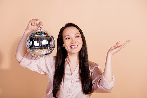Photo of lovely pleasant girl wear pink shirt holding discoball palm presenting event empty space isolated on pastel color background.