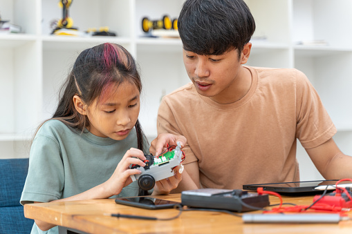Young girl trying to assembly her robot kit while her young male instructor sitting next to her helping out