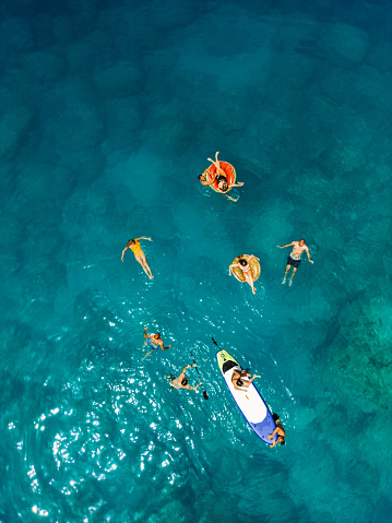 People swimming and floating around standup peddle board in amazing clear sea water with beautiful beach. Lefkada island, Porto Katsiki bay and beach, Greece