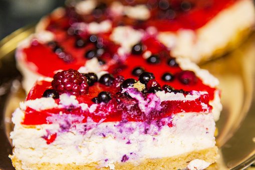 Slice of cheese cake with black currant berries on a table in a white plate.