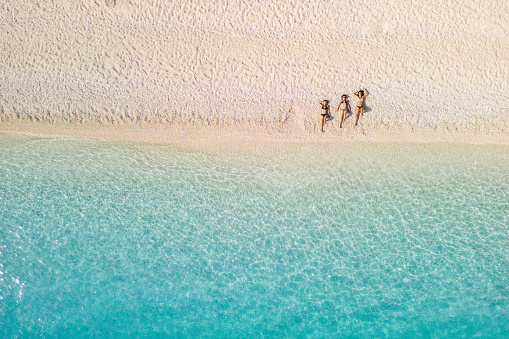 Three women enjoying sunbathing at morning on the beach with in crystal clear water with beautiful color. Famous Fteri beach, island of Kefalonia, Greece
