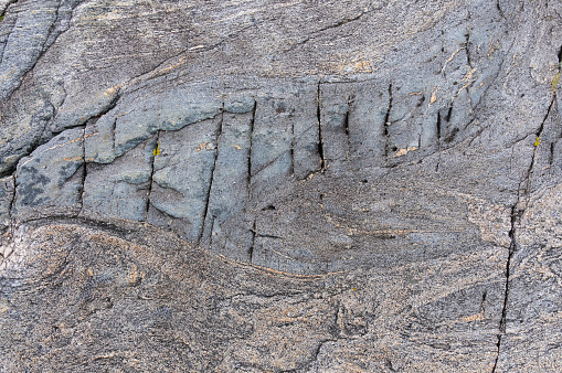 Close-up of historical carvings etched into a grey rock face, with natural patterns visible.