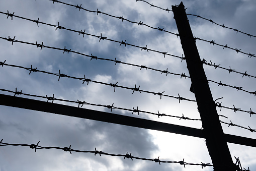 Barbed wire on the fence. Background of cloudy sky.