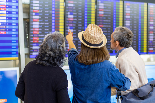 Group of Asian family tourist passenger with senior parent looking at the departure table at airport terminal for airline travel and holiday vacation