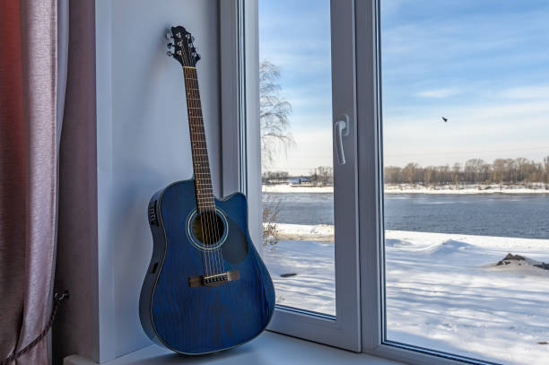 Dreadnought acoustic guitar is on window sill by the window.