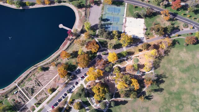 A 4K drone shot over Washington Park and Tennis Courts, Mount Vernon Garden, and Grasmere Lake, in Denver, Colorado, on a peaceful day, during the colorful Fall season.