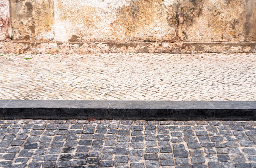 A side view of an old fashioned and weathered cobbled street, stone curb, and pavement in Lisbon.