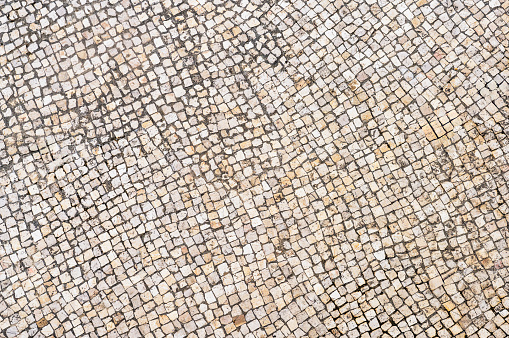 A view from directly above a large area of outdoor stone pavement tiles in Lisbon, Portugal, weathered with use and age.