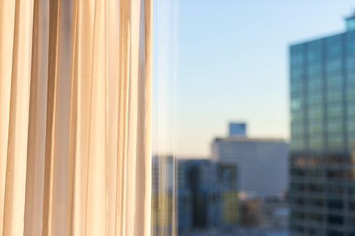 A morning view of curtains illuminated by sunshine, with the office towers of downtown Philadelphia, defocused in the distance.