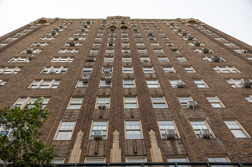 Manhattan, NY, USA–September 22th, 2023: Frog's perspective of a symmetrical facade of a brick residential building. Outdoor air conditioning units hang near the windows