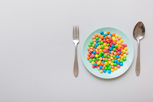 cutlery on table and sweet plate of candy. Health and obesity concept, top view on colored background.