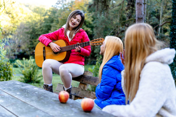 Three friends enjoy the beauty of nature on a bench, with one of them skillfully playing the guitar for a soothing experience