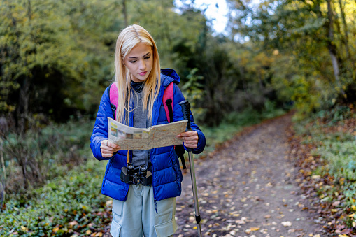 The image captures a woman confidently navigating the trail by reading a map, showcasing her skills as a trailblazer and emphasizing her self-assured approach to hiking