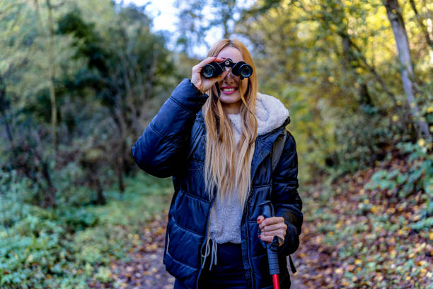 The photo captures a woman on a hiking trail using binoculars to magnify the breathtaking vista, highlighting her keen interest in observing the natural surroundings and making the most of her outdoor adventure